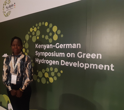 Lucy Ombaka standing infront of a poster of the Kenyan-German Symposium on Green Hydrogen Development